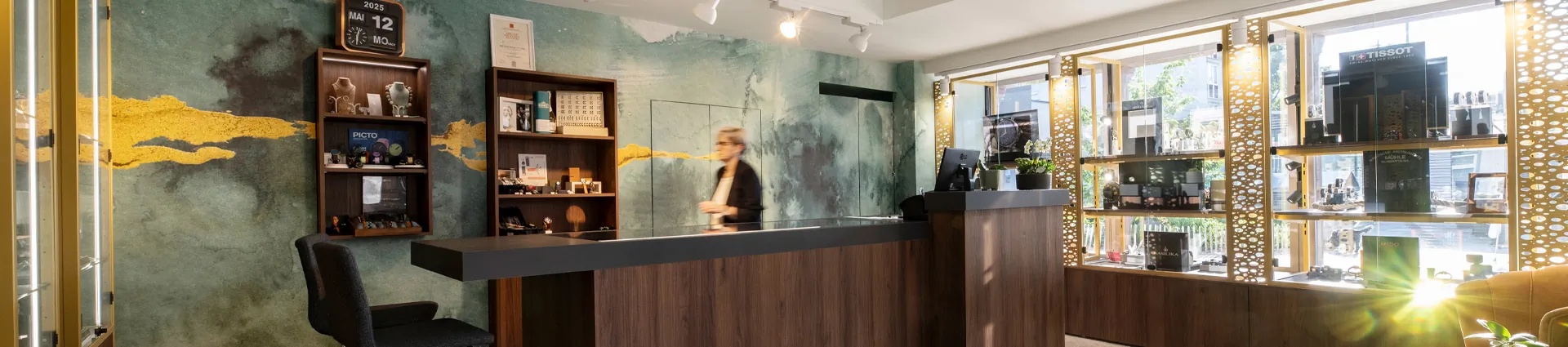 Innenansicht des Juweliergeschäfts Zeit-Punkt mit Empfangstheke, modernem Wanddesign und sonnendurchfluteter Auslage mit Uhrenmarken wie Tissot und Mido