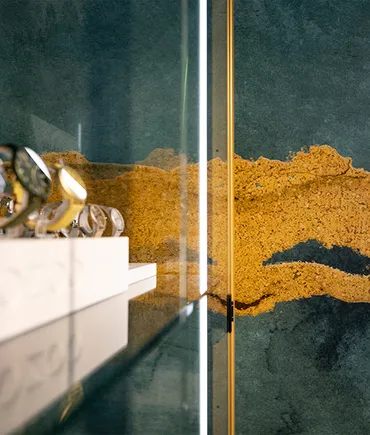 Nahaufnahme einer Glasvitrine mit edlen Uhren und goldener Wandstruktur im Hintergrund
